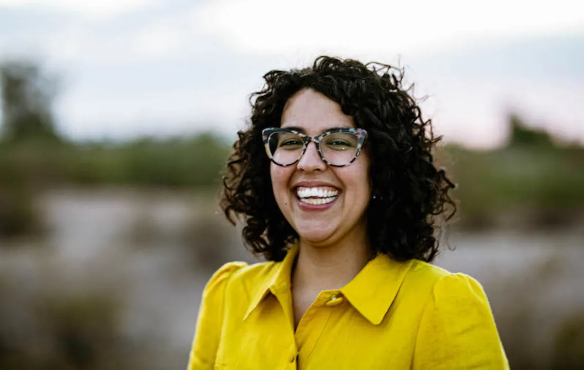 smiling woman wearing glasses and bright yellow outfit outdoors