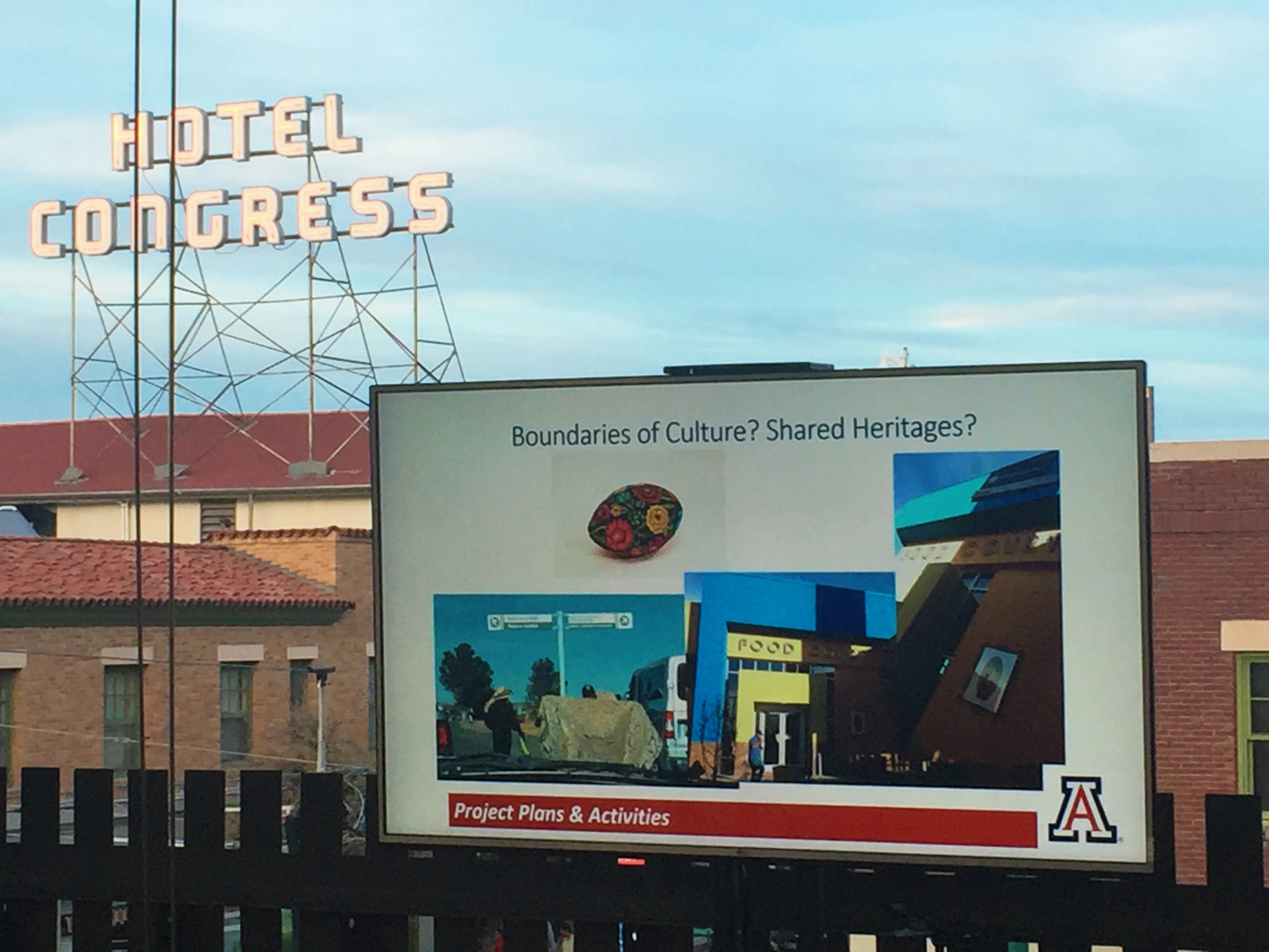 Hotel Congress neon sign above and behind a projection screen with a message about borders