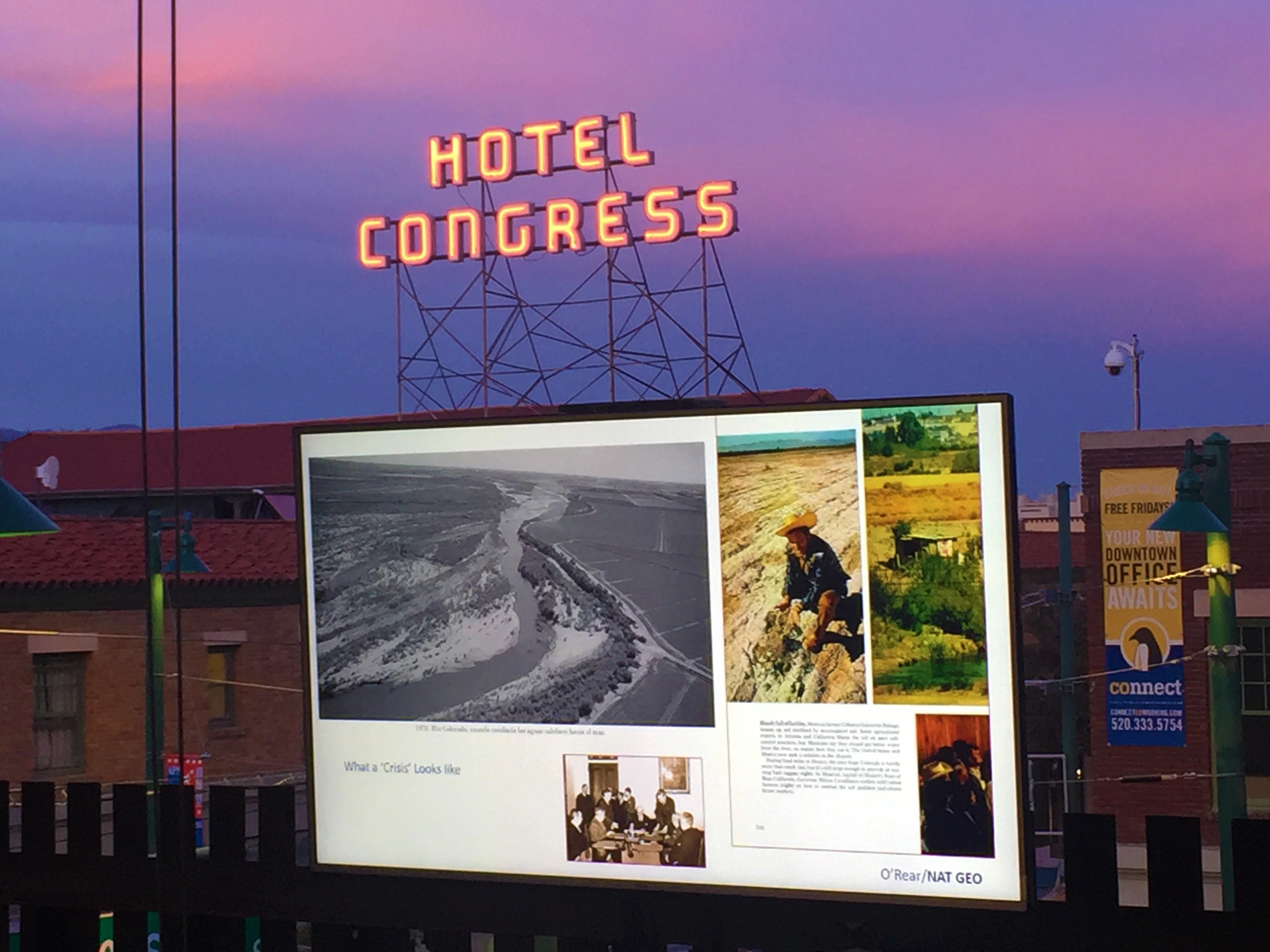 Hotel Congress neon sign above and behind a projection screen with a message about borders