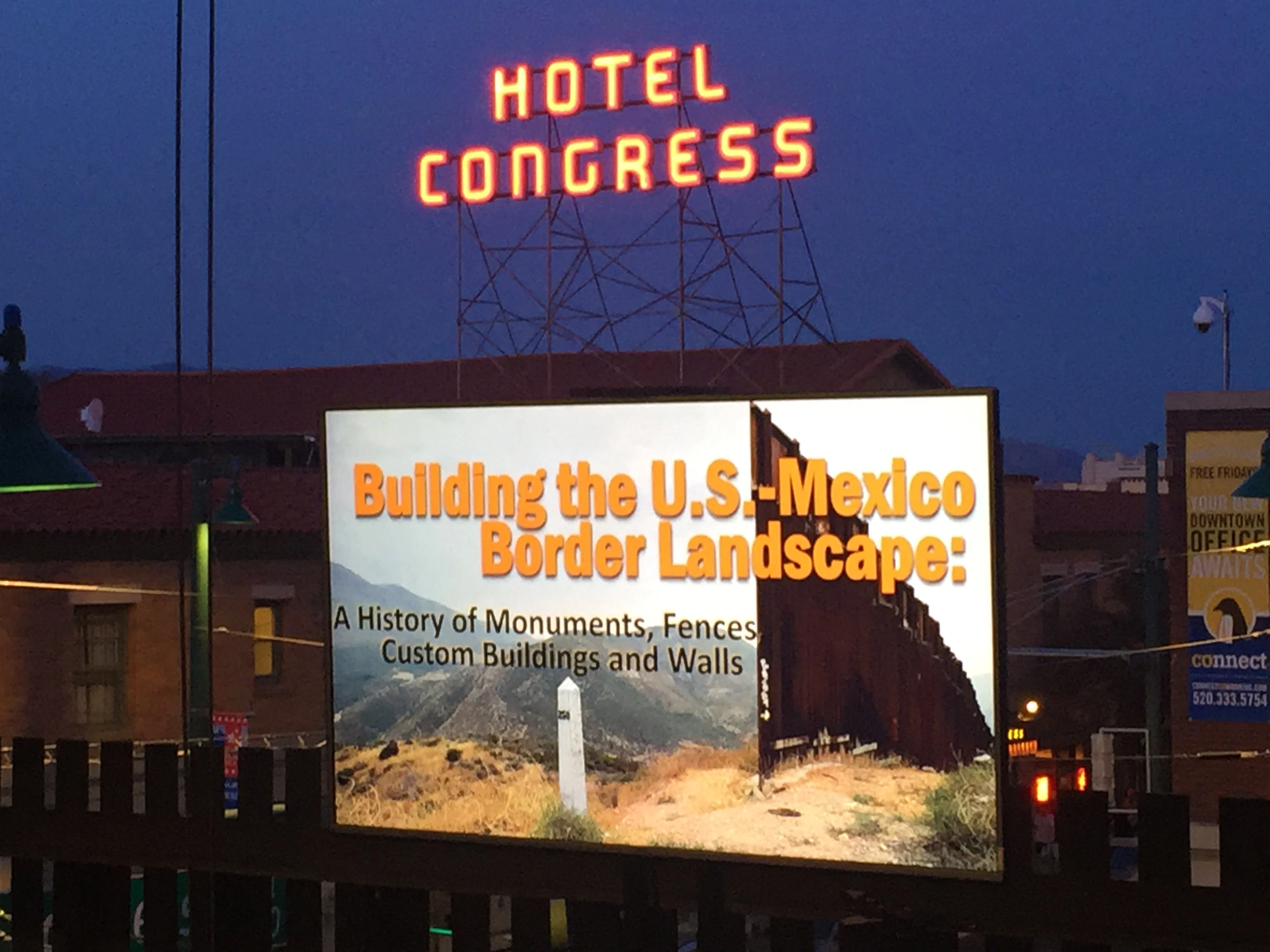 Hotel Congress neon sign above and behind a projection screen with a message about borders
