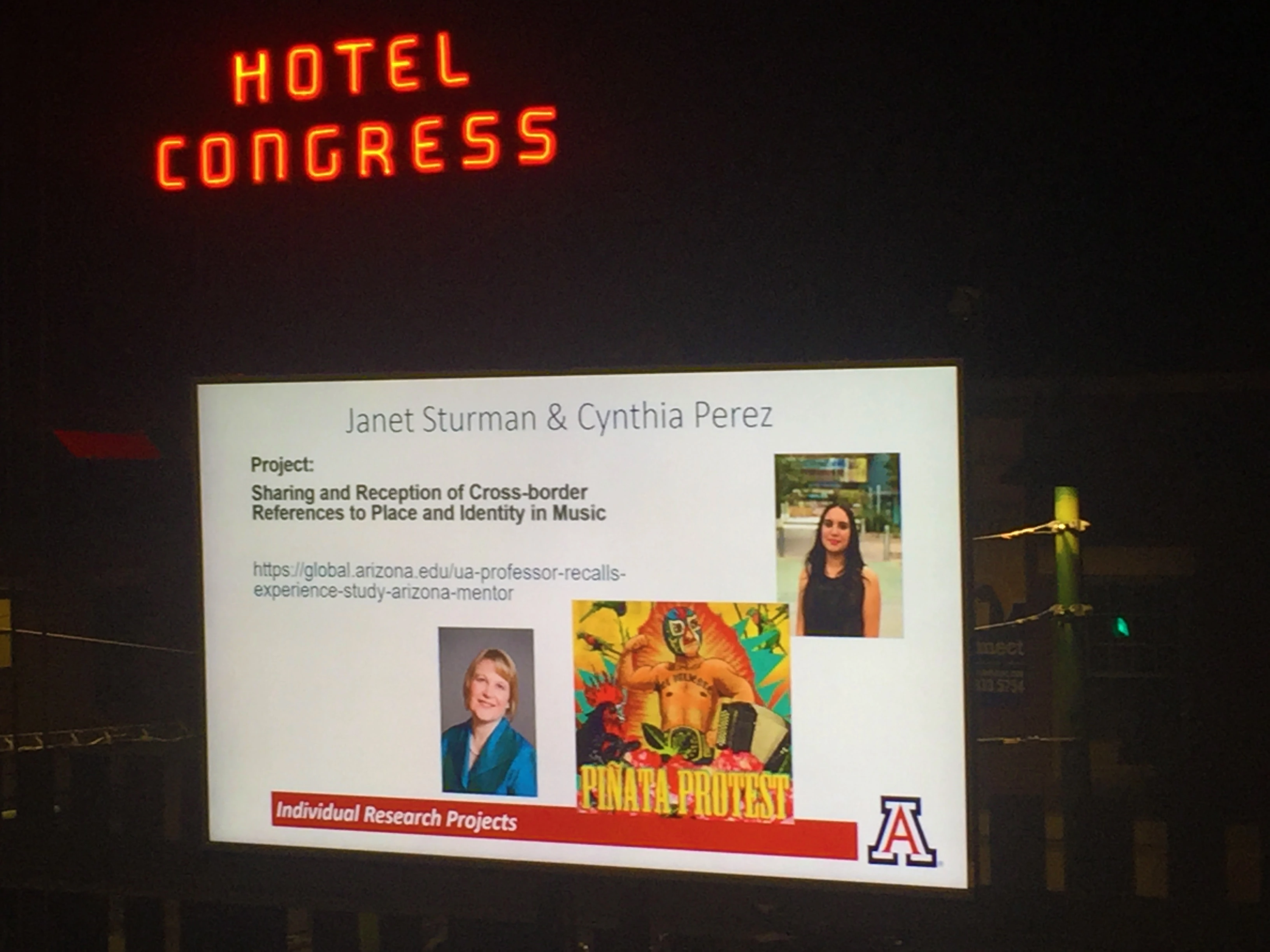 Hotel Congress neon sign above and behind a projection screen with a message about borders