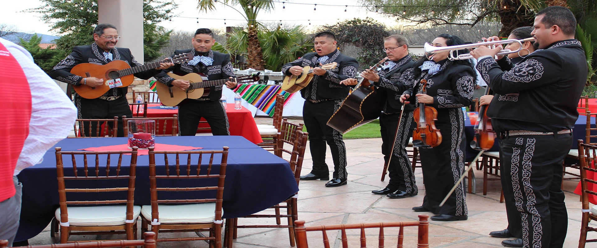 A mariachi band playing before a crowd of people at picnic tables.